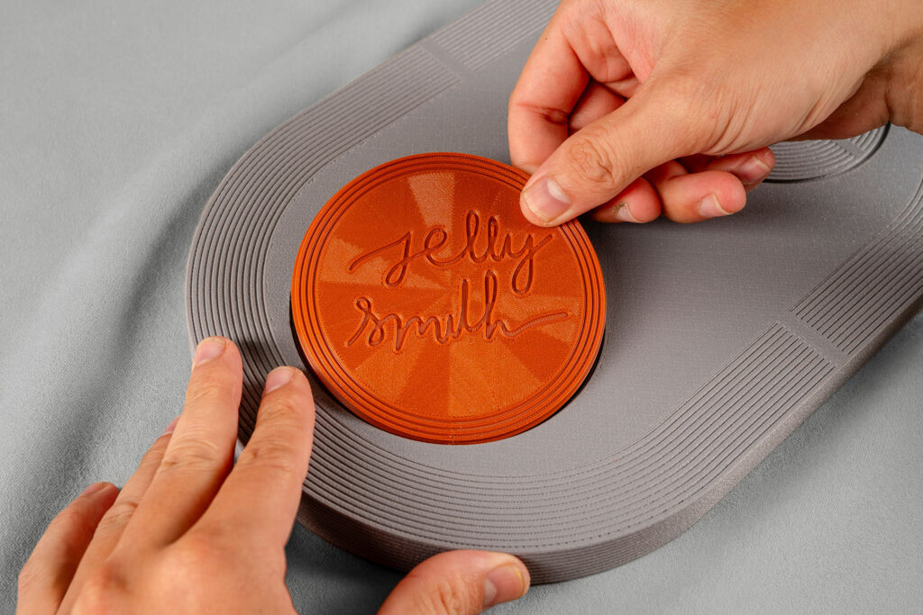 A hand fitting the engraved Jelly Smith logo disc into the base of a Drop EDC Tray