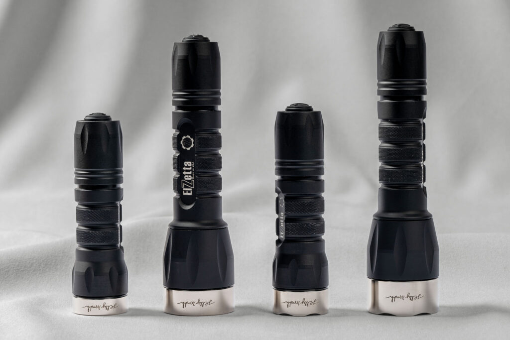 Four Elzetta flashlights standing upright, each fitted with a Jelly Smith stainless steel bezel